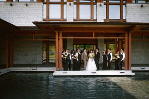 Wedding party poses on a modern pool deck outside a contemporary stone and wood venue.