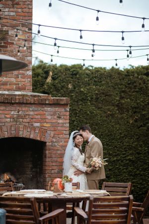 An intimate wedding moment by a brick fireplace under string lights.