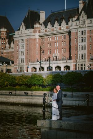 Couple shares romantic wedding moment on waterfront steps with grand historic Empress Hotel in Victoria, BC as backdrop.
