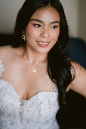 A bride in a white lace strapless wedding dress smiles while wearing a delicate initial necklace and earrings.