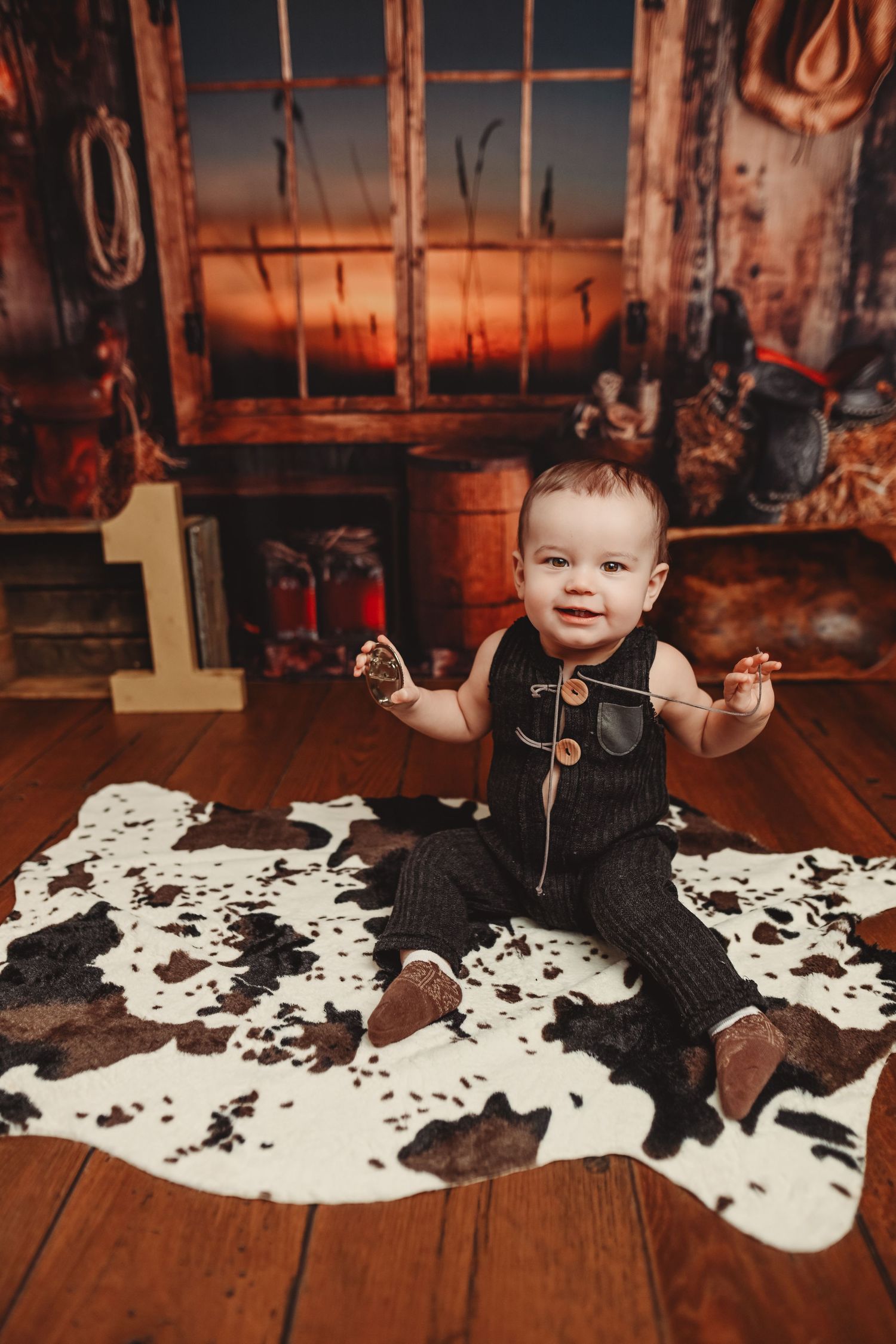 Rustic baby photography with cowhide rug on wooden floor at sunset.