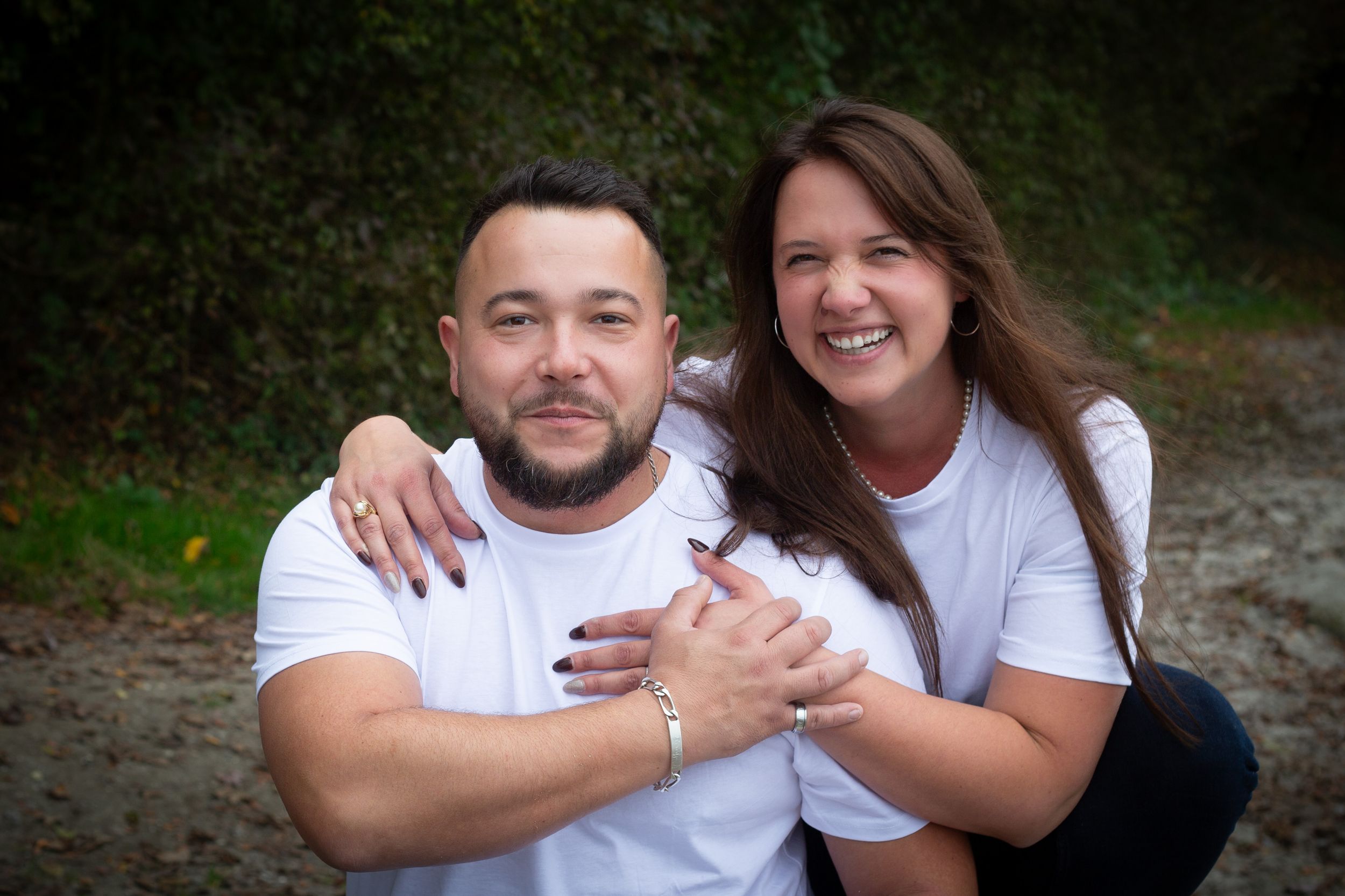 Couple in white t-shirts sharing a loving embrace outdoors with natural background.