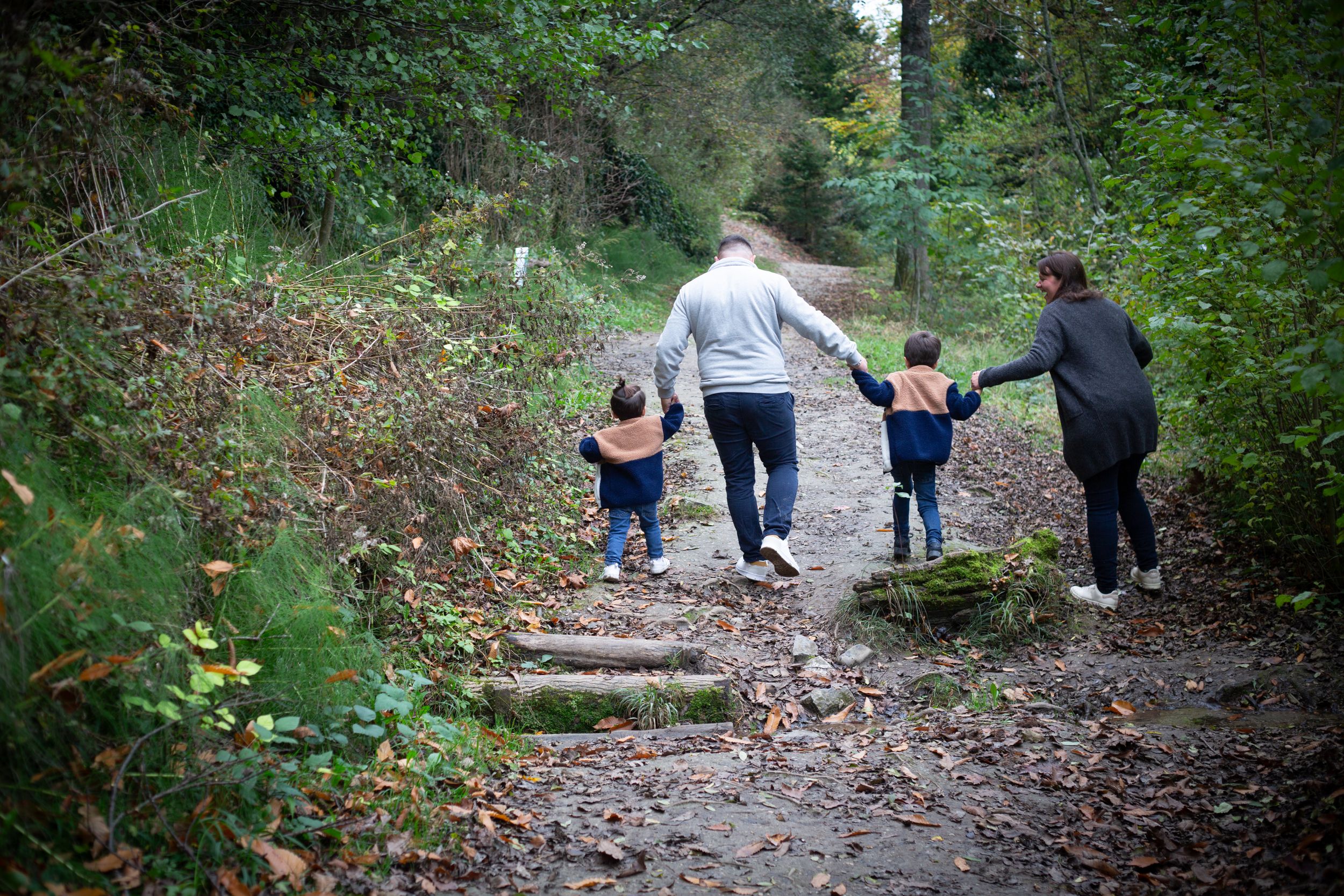 Family walking together on a forest trail holding hands on an autumn day.