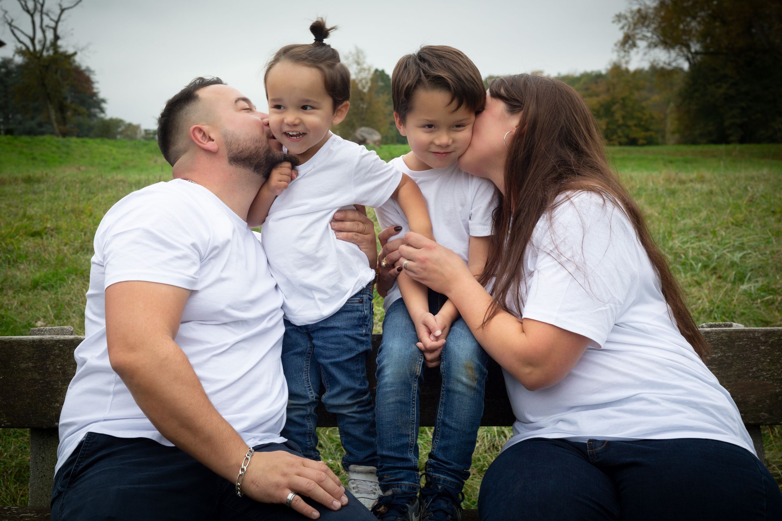 Family portrait outdoors with everyone wearing matching white shirts showing affection.