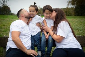 Family portrait outdoors with everyone wearing matching white shirts showing affection.