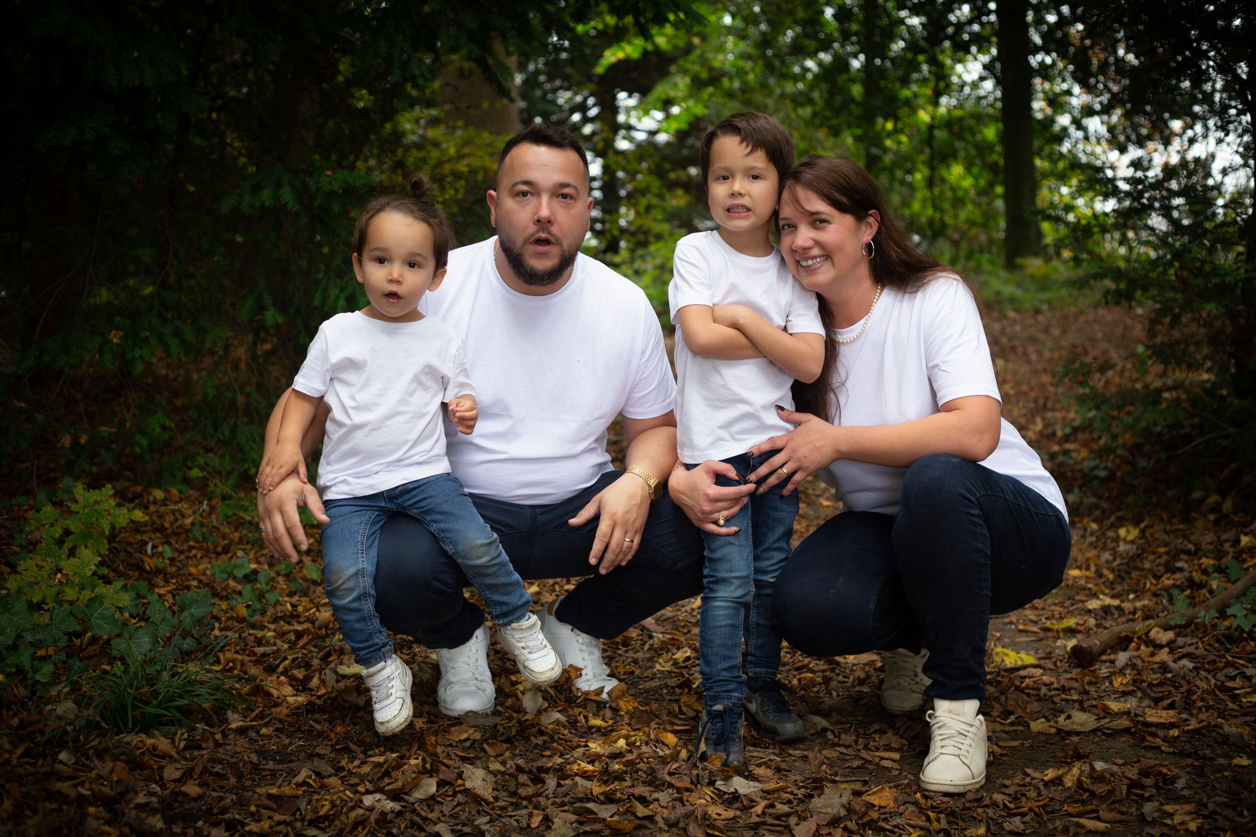 Family group portrait in matching white t-shirts sitting together in wooded setting.