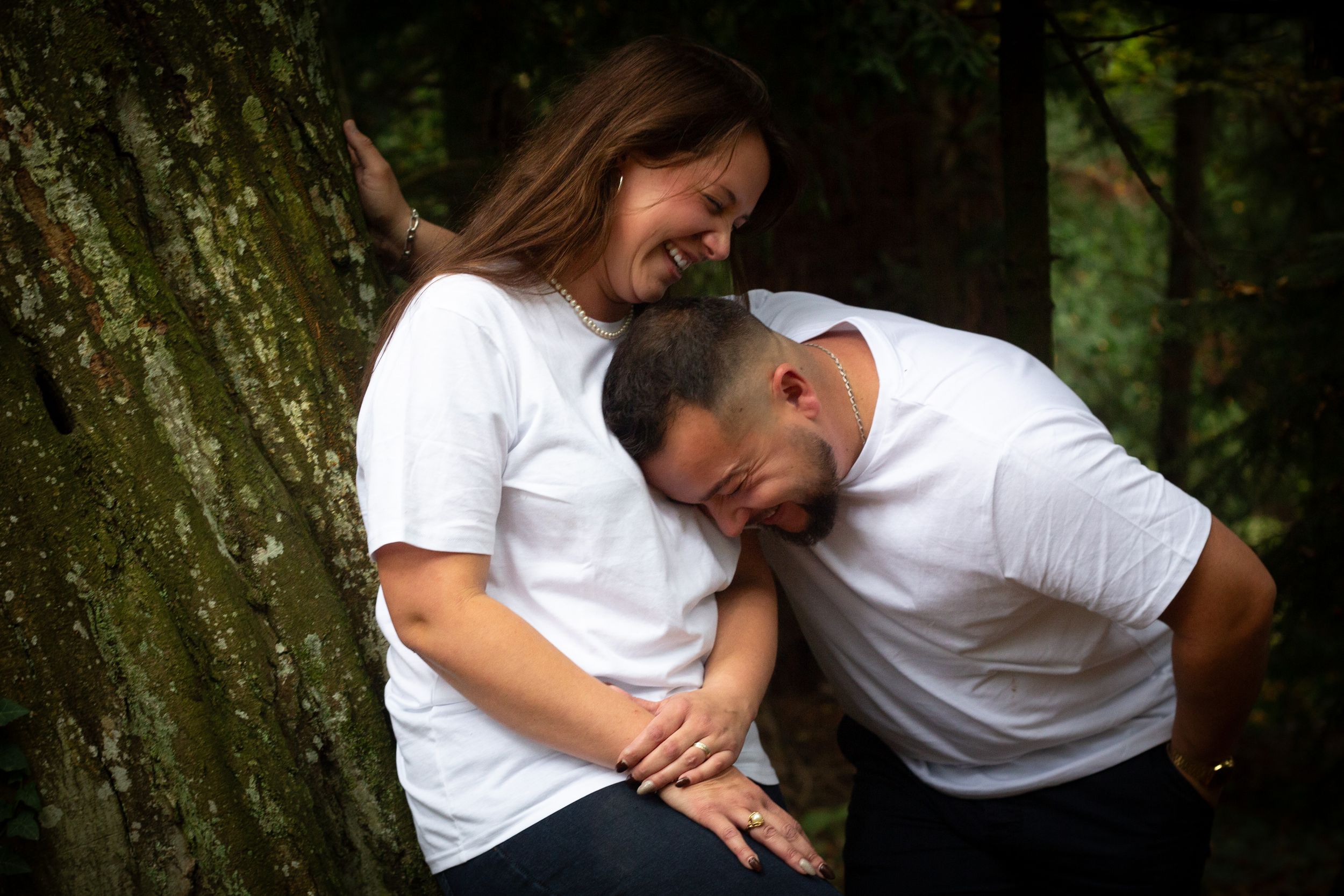 Couple sharing intimate moment and laughter while leaning against tree trunk.