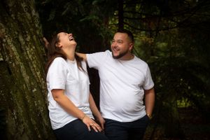 Candid moment of couple laughing together while posing by large tree trunk.