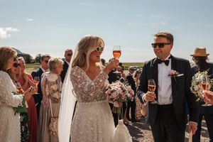 A group of people socializing at an outdoor wedding reception with drinks and conversation on a sunny day.