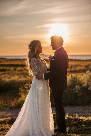 Newlyweds share an intimate moment at sunset in a golden field wearing wedding dress and suit.