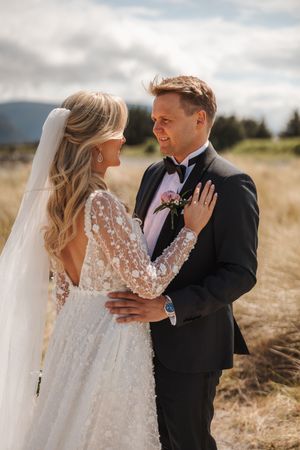Newlyweds share an intimate moment in a rustic field with mountains in the background on their wedding day.