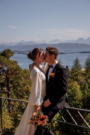 A romantic wedding couple share a kiss on a scenic mountain overlook with ocean views and mountains in the background.