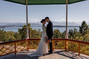 A couple embraces in a romantic moment on a mountaintop gazebo overlooking snow-capped mountains and a scenic lake.