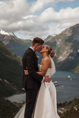 A couple shares an intimate wedding moment against the dramatic backdrop of a Norwegian fjord and snow-capped mountains.