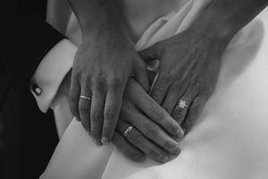 Black and white photo showing elegant hands wearing wedding rings resting on white fabric.
