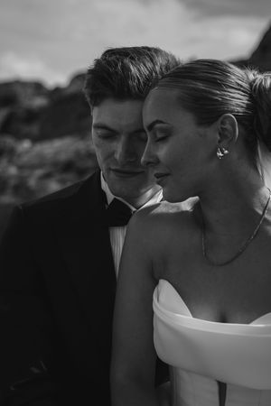 Close intimate moment between newlyweds in black and white, bride wearing elegant off-shoulder wedding dress.