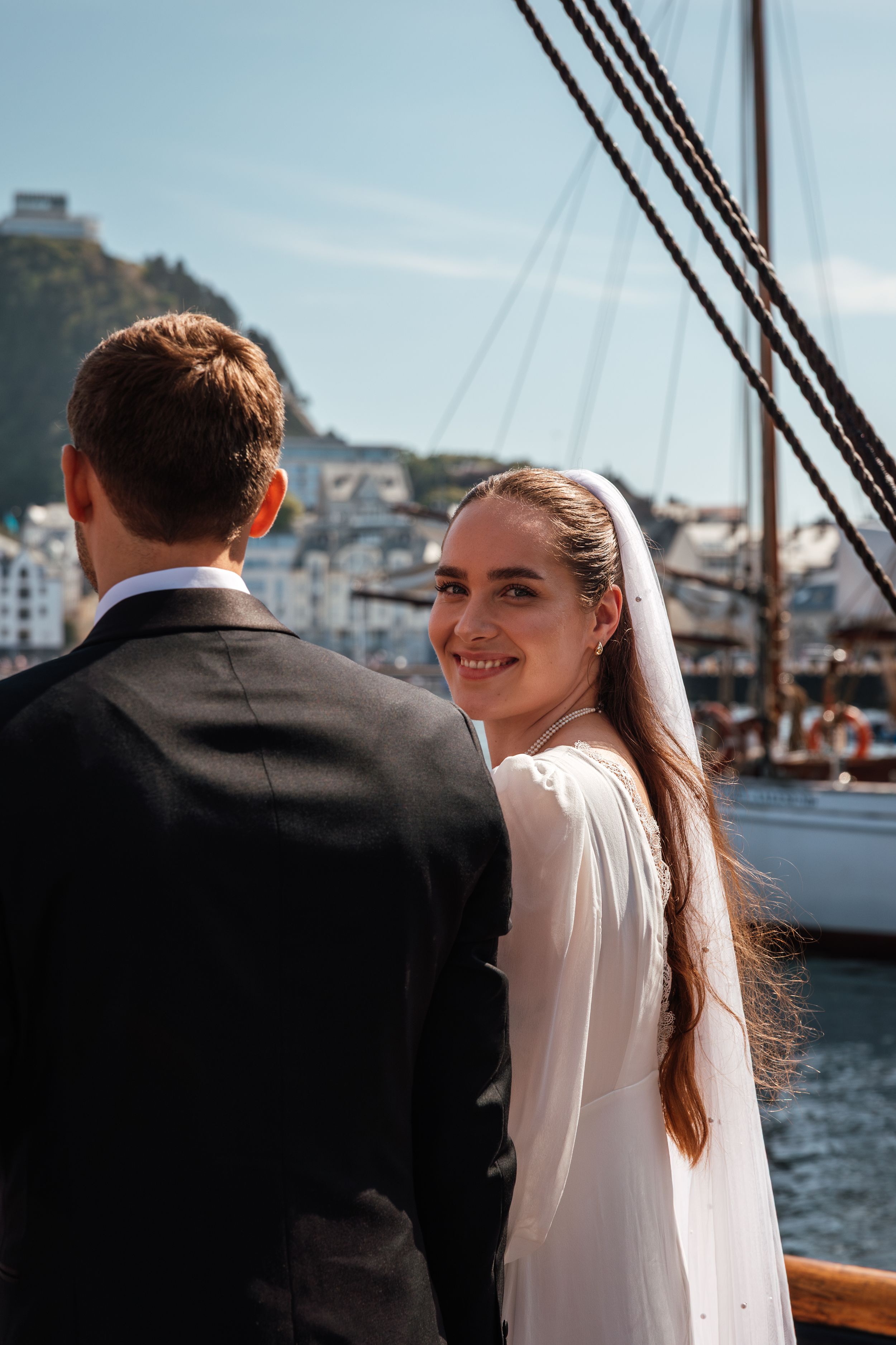 Couple enjoying scenic harbor views from aboard a classic yacht in elegant wedding attire.