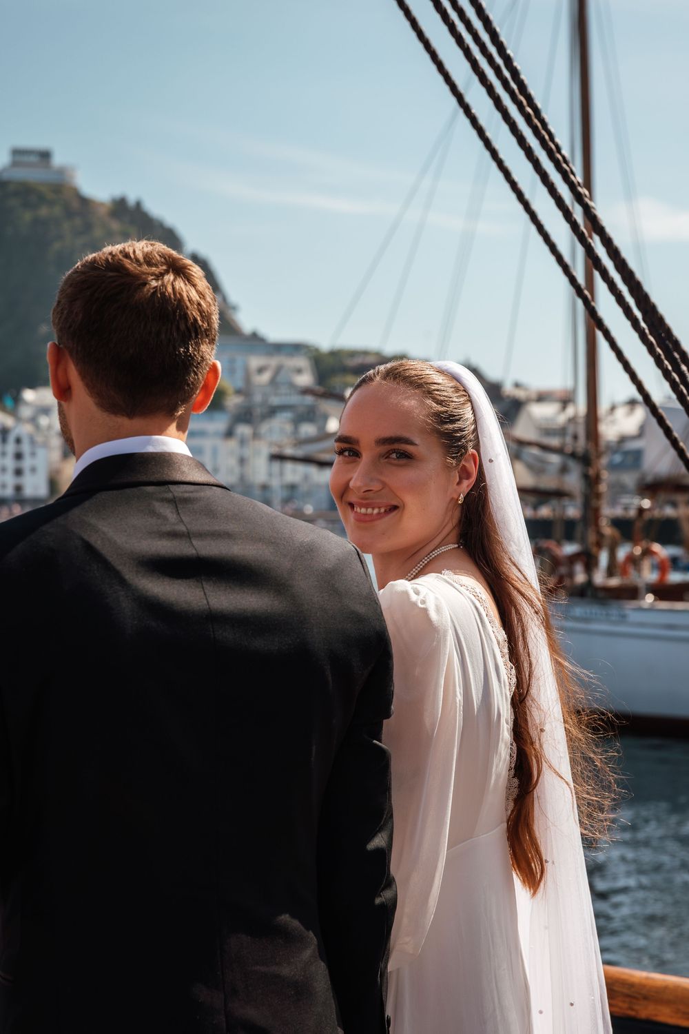 Couple enjoying scenic harbor views from aboard a classic yacht in elegant wedding attire.