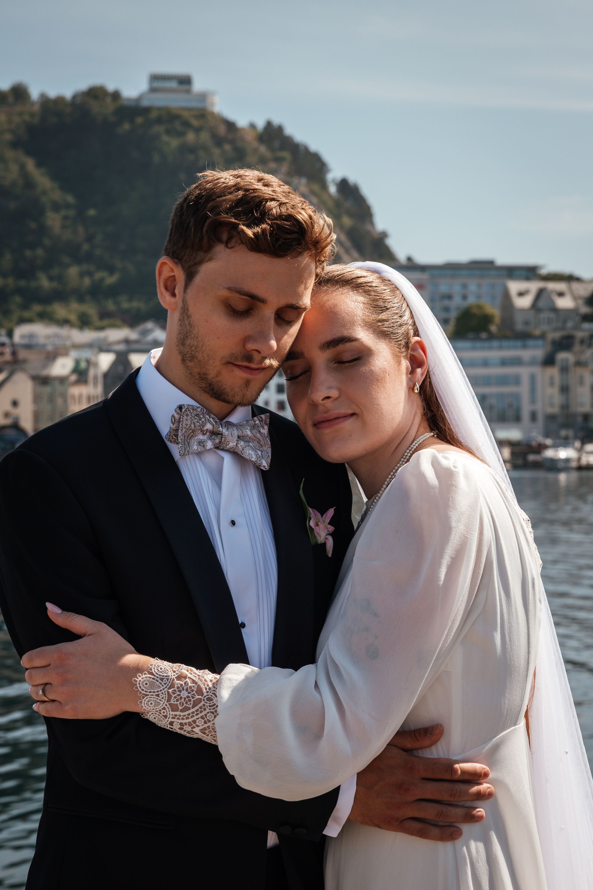 A couple shares intimate wedding day moments in elegant attire by the waterfront at sunset.