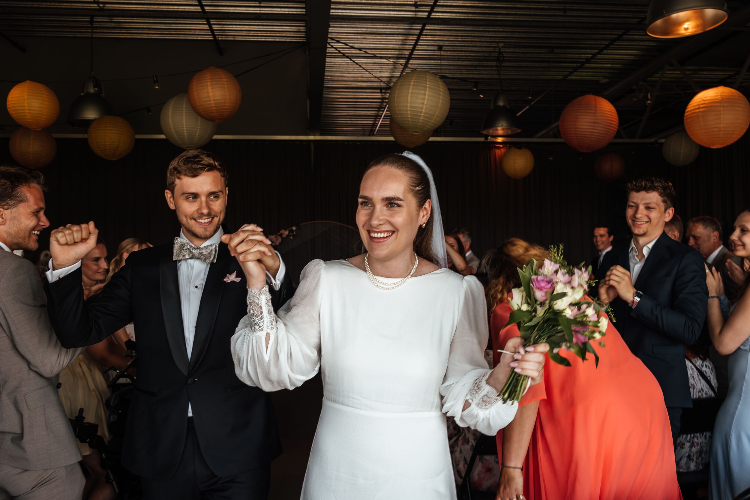 A joyous celebration on a dance floor with round paper lanterns overhead and guests cheering in the background.
