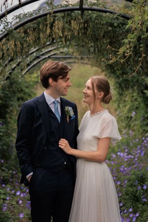 A couple shares a joyful moment together in a garden with purple flowers and greenery.