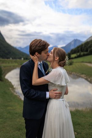 A romantic wedding couple embraces in a scenic mountain valley with a winding river and green meadows.