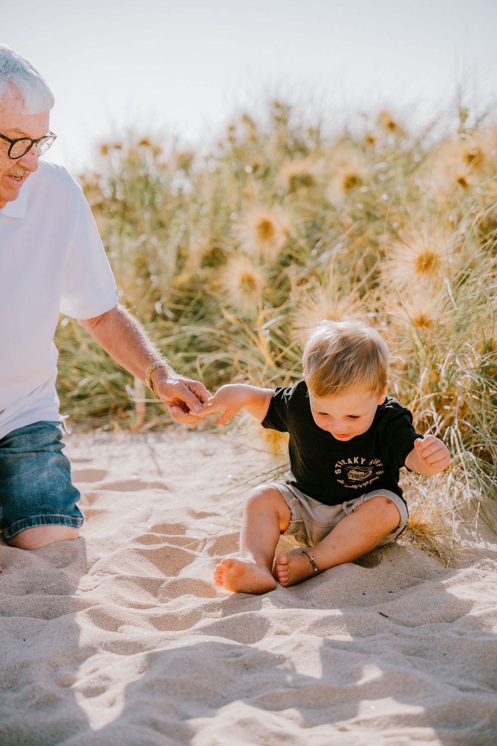 Child playing and rolling in soft beach sand during a sunny day.