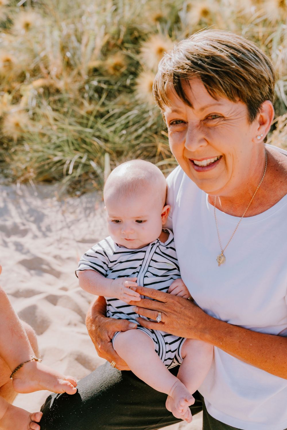 Sweet candid moments between a baby in striped outfit and loved one at the beach.
