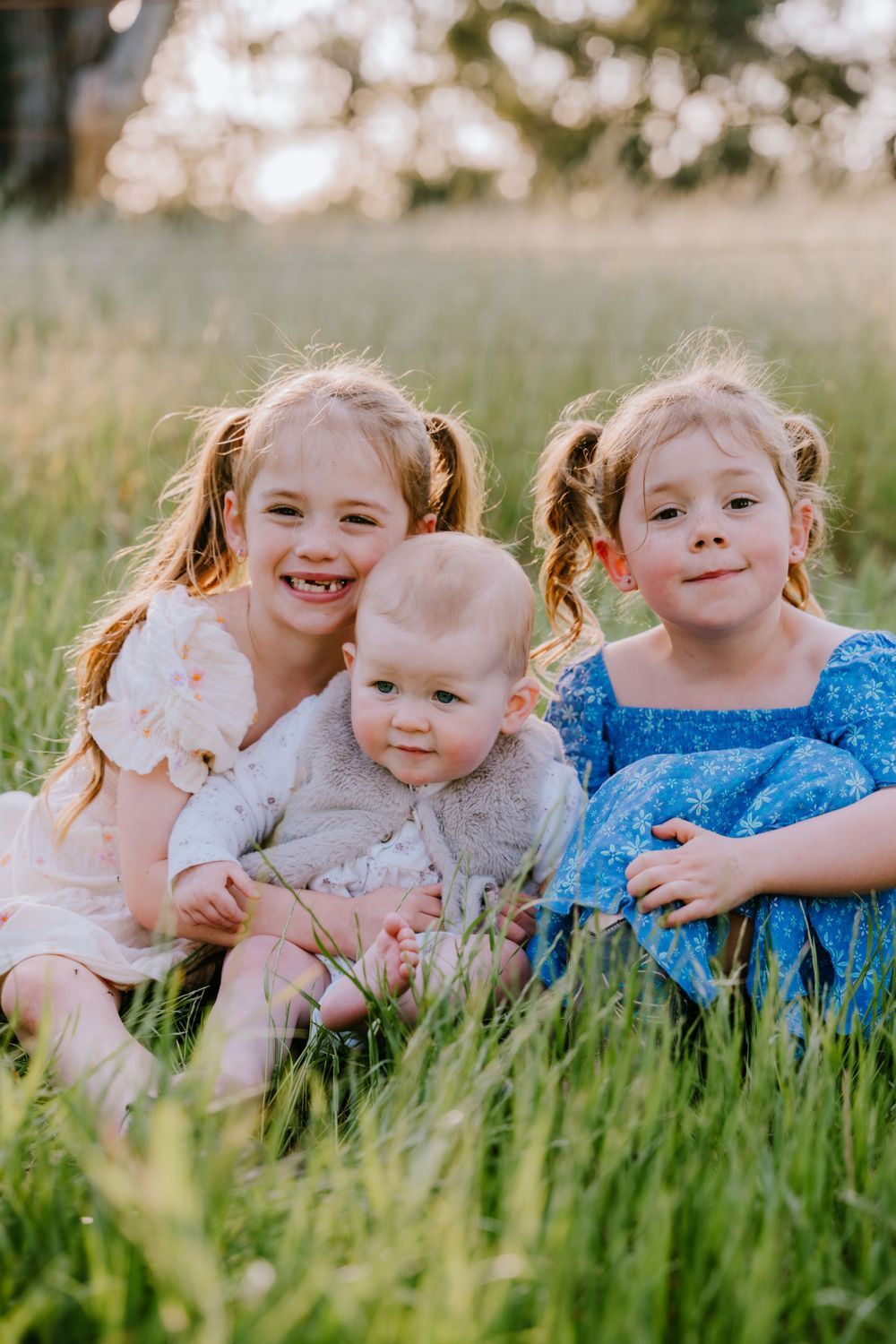 Children in colorful dresses lay together in tall grass during a golden hour photoshoot.