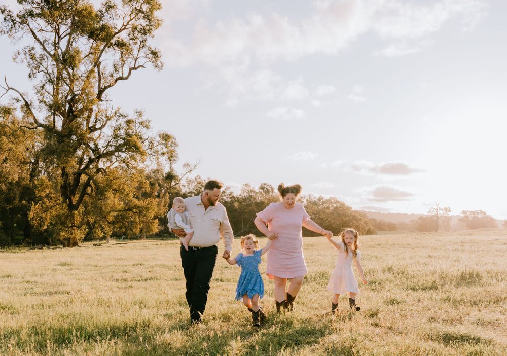 Wide landscape shot of family walking together across open field at sunset.