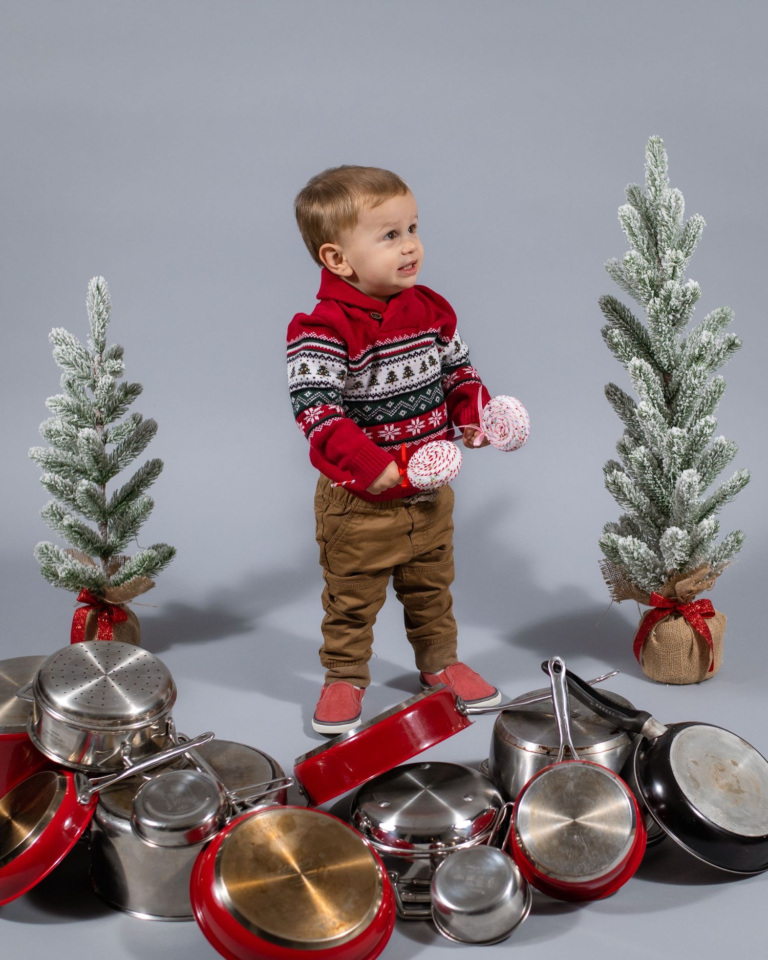 Festive holiday portrait with small decorative trees and wooden stool against gray backdrop.