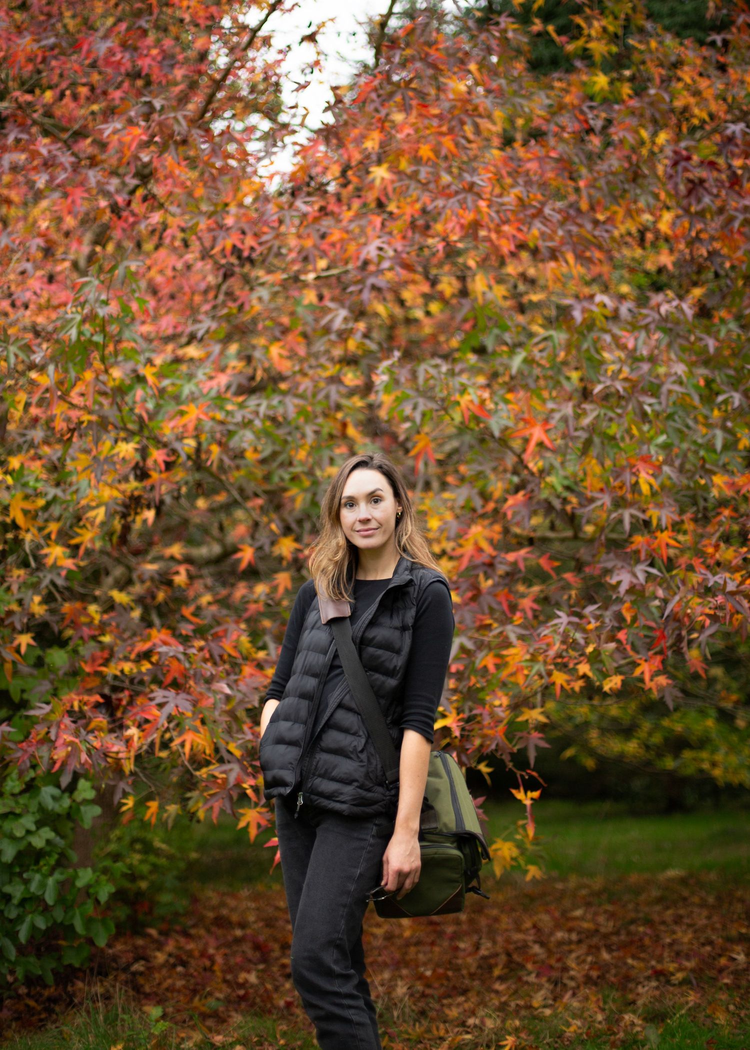 Fall portrait session featuring dark outfit against vibrant autumn foliage background.