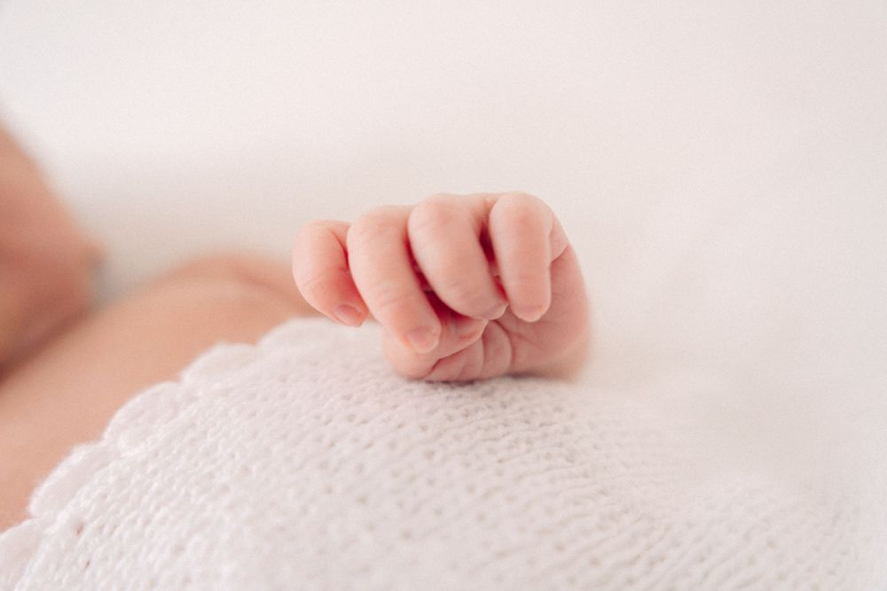 Close-up macro shot of delicate newborn baby fingers against white textured fabric.