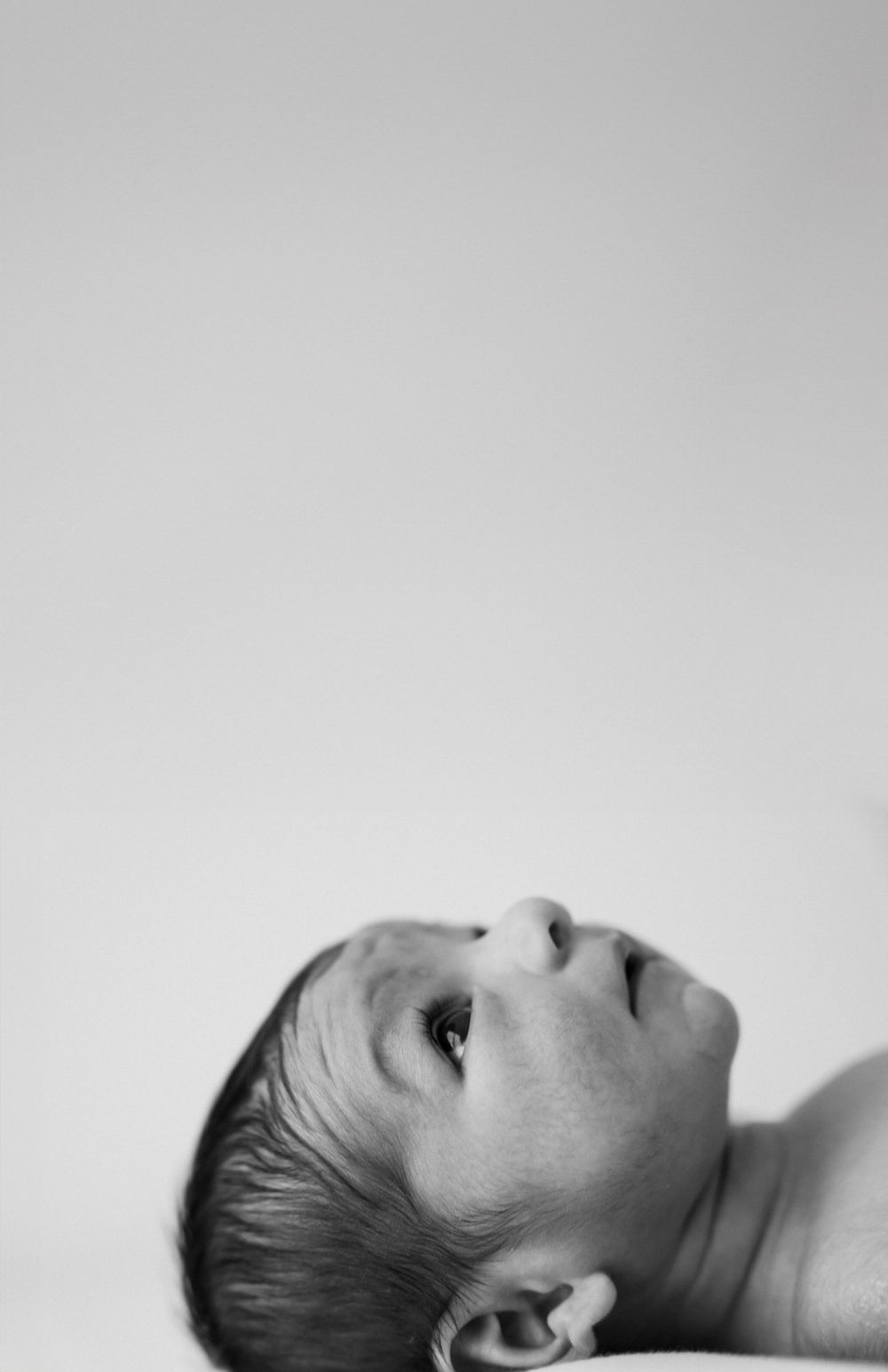 Black and white close-up portrait of an infant's face looking upward against a light background.