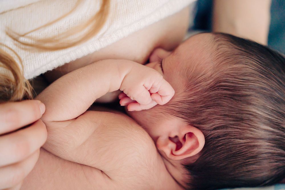 Tender moment with newborn baby swaddled in white during professional photo session.
