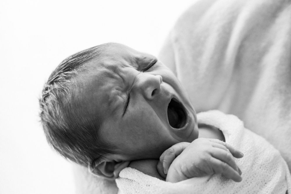 Black and white portrait of a yawning newborn wrapped in soft fabric.