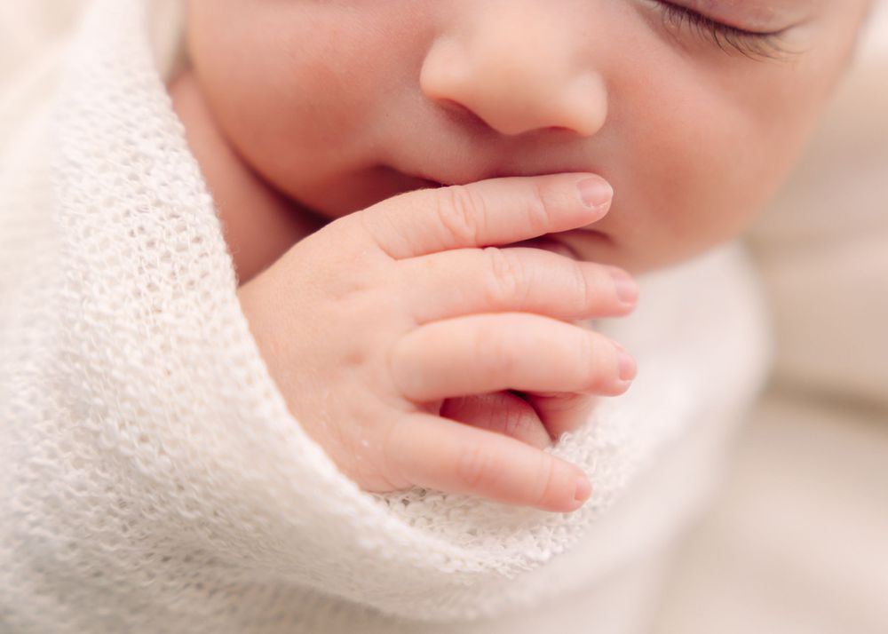 Delicate close-up of a sleeping baby's face and hand against soft fabric.