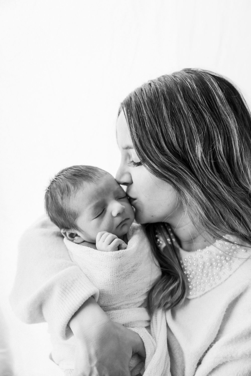 A tender moment between parent and newborn swaddled in white.