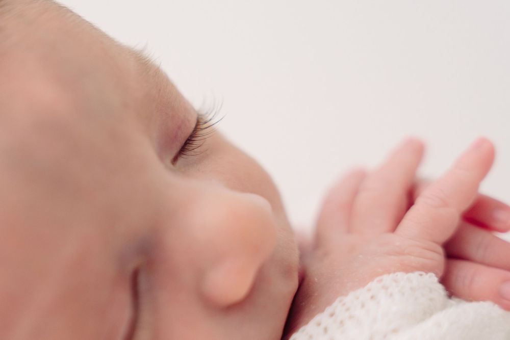 Close-up of a sleeping newborn's face and tiny hand wrapped in white fabric.