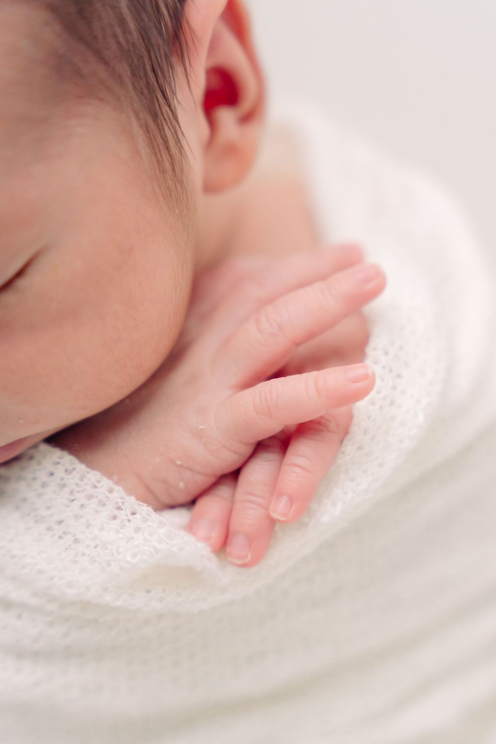 Close-up of tiny newborn hands resting against soft white textured fabric.