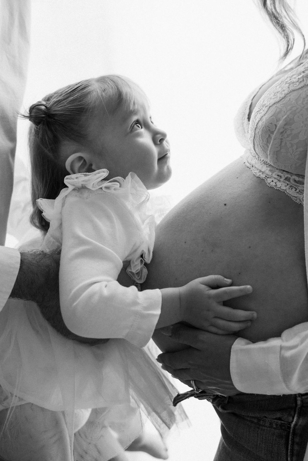 Young child touches expectant mother's belly in tender black and white portrait.
