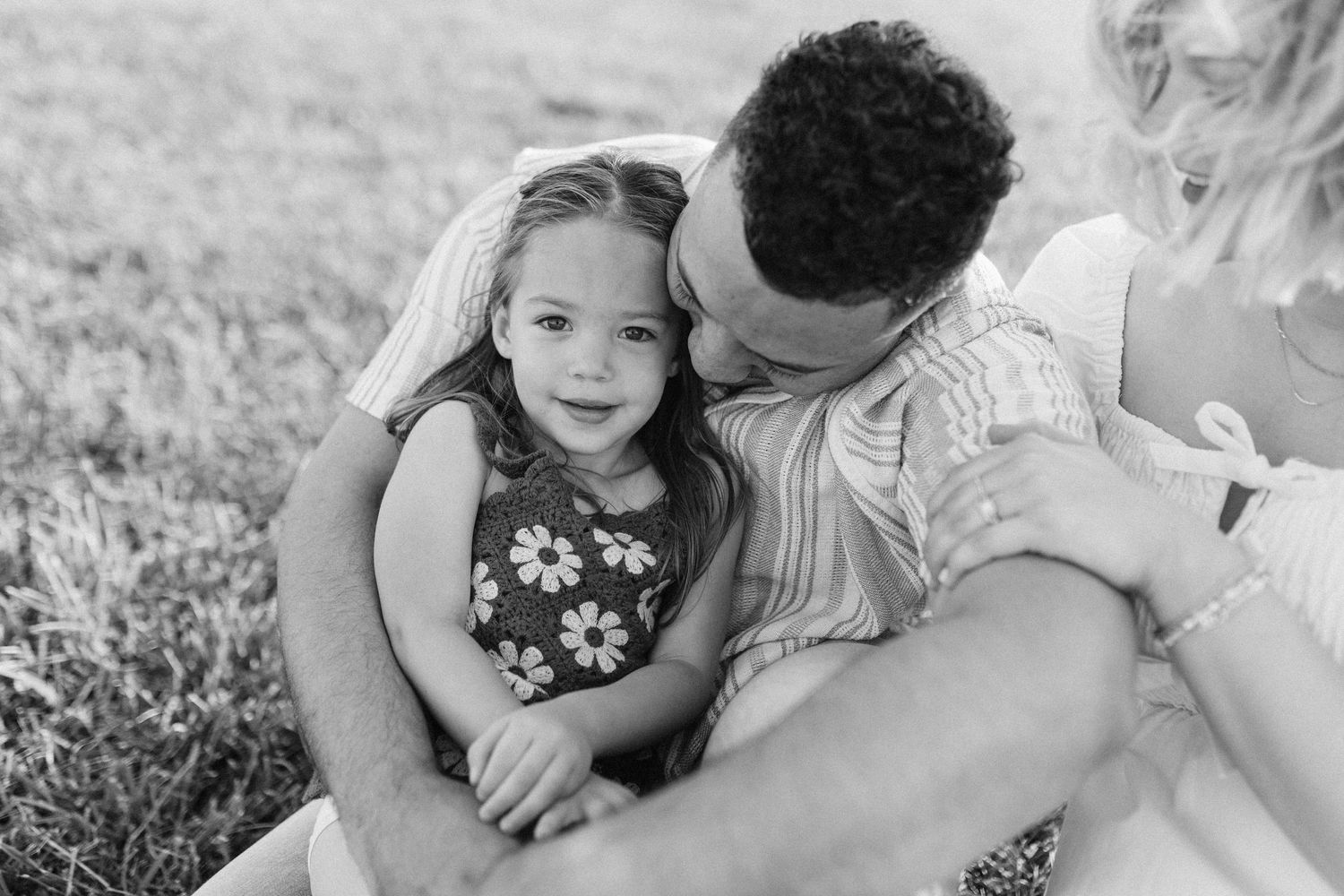 Black and white photo of a tender parent-child moment captured in a grassy field during a sunny day.