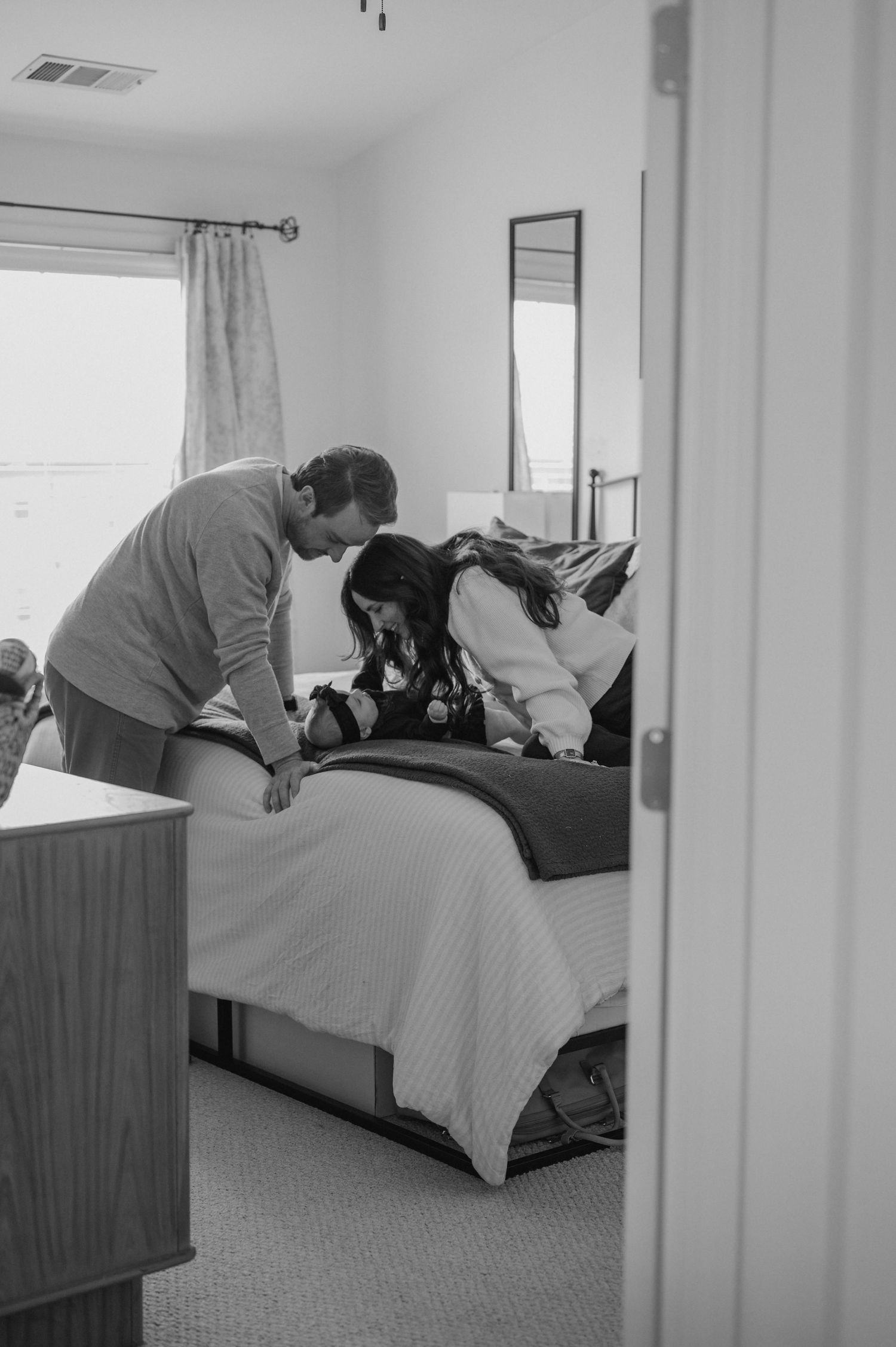 A candid black and white photo showing a couple preparing in a bedroom.