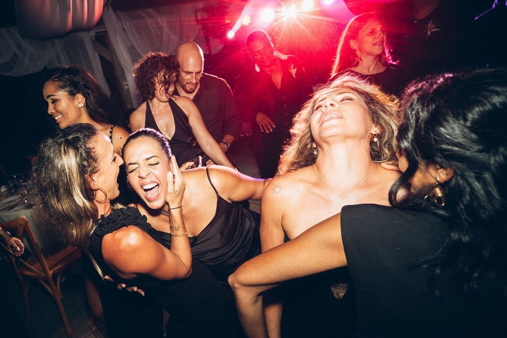 Group of young women dancing and laughing together at a lively nightclub party with colorful stage lighting.