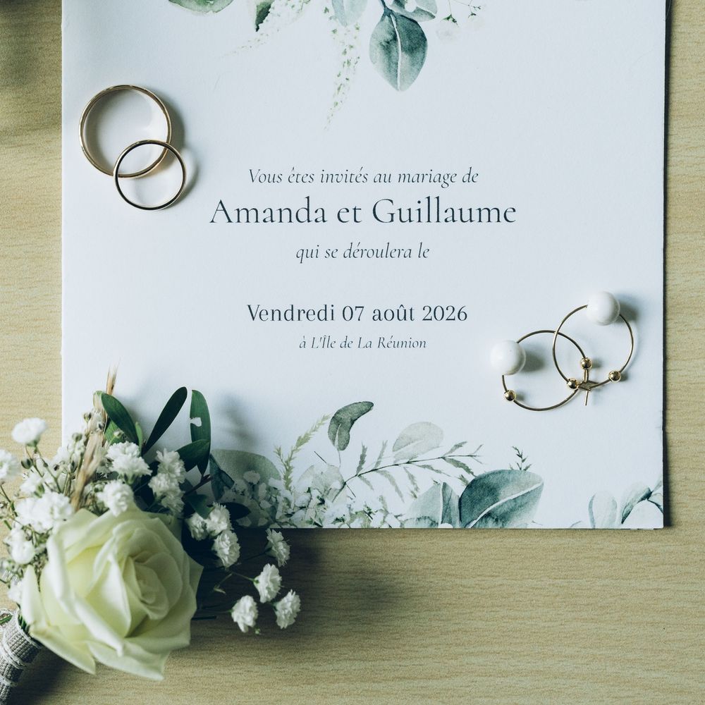 Elegant French wedding invitation for Amanda et Guillaume on August 7, 2026, with gold rings, earrings, and white flowers.