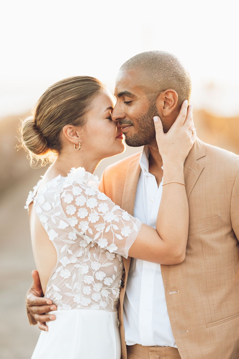 Romantic wedding couple embraces in golden sunlight wearing elegant attire.