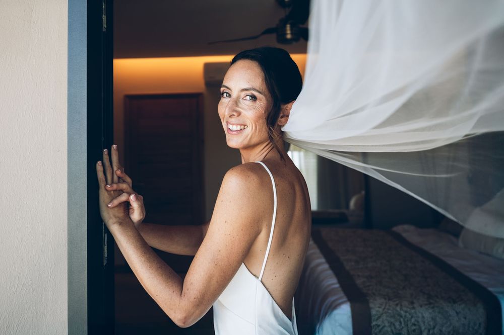 Bride in a white wedding dress turns around and smiles with flowing veil in softly lit room.