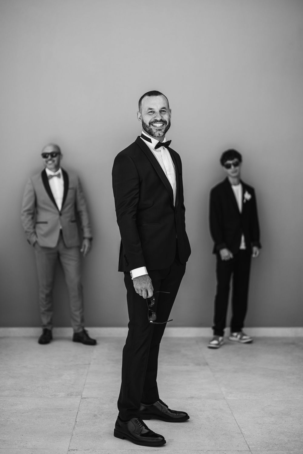 Black and white photo series showing different views of figures in formal attire standing against a plain wall.