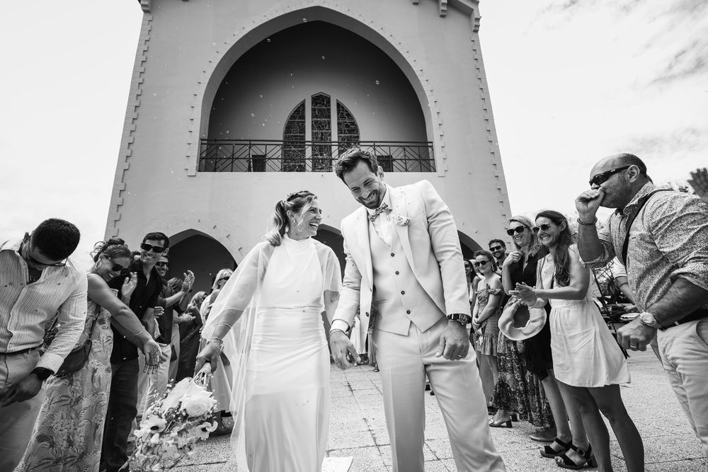 Wedding guests lined up along white stucco wall tossing rose petals during outdoor celebration.