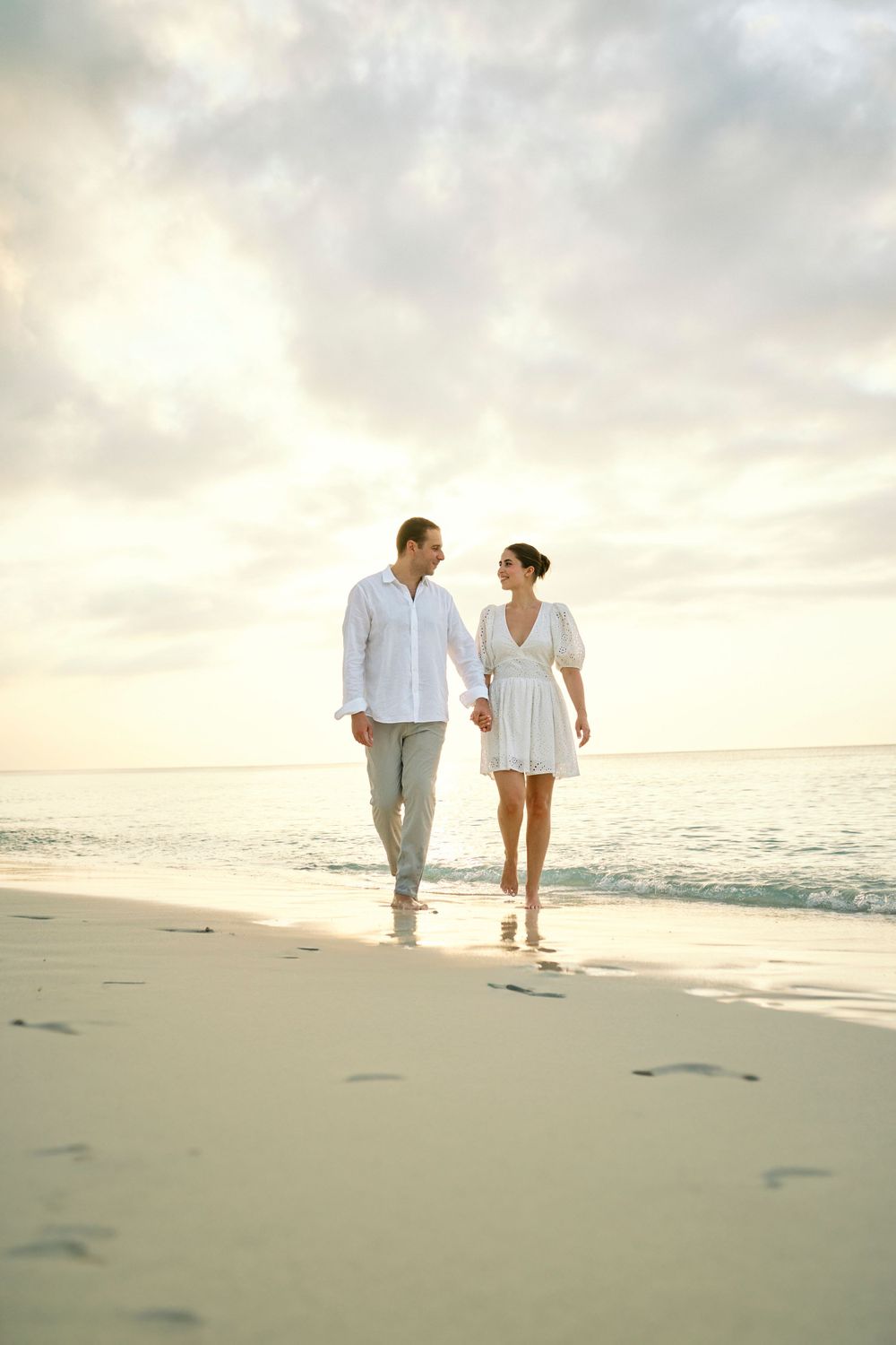 Romantic couple walking together on a sunset beach in light casual attire.